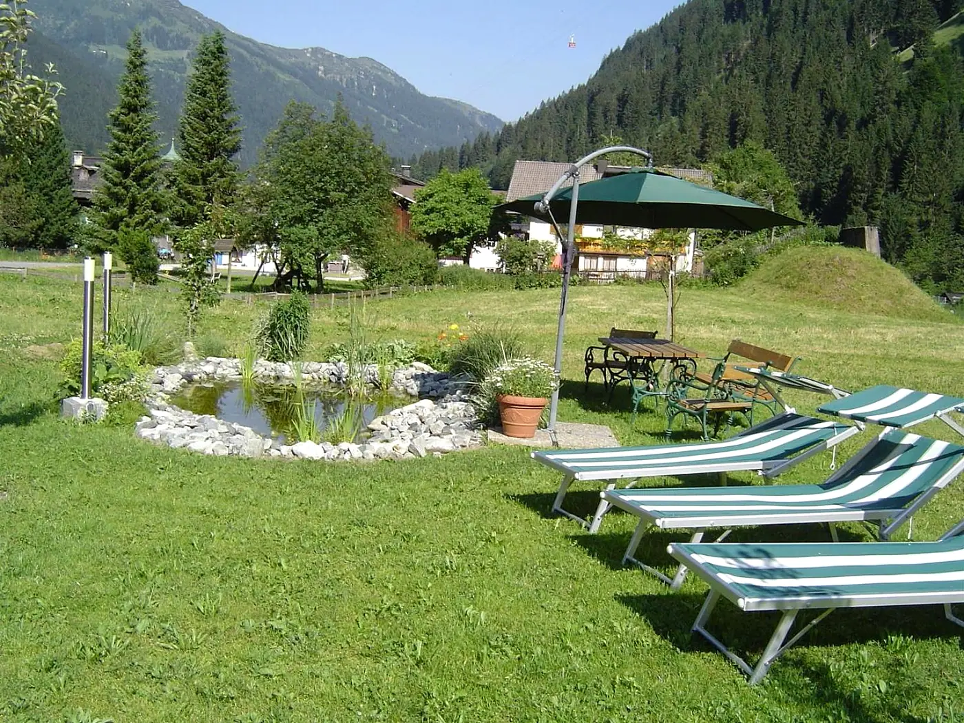 Liegestühle am Teich im Garten, dahinter Wald und Berge