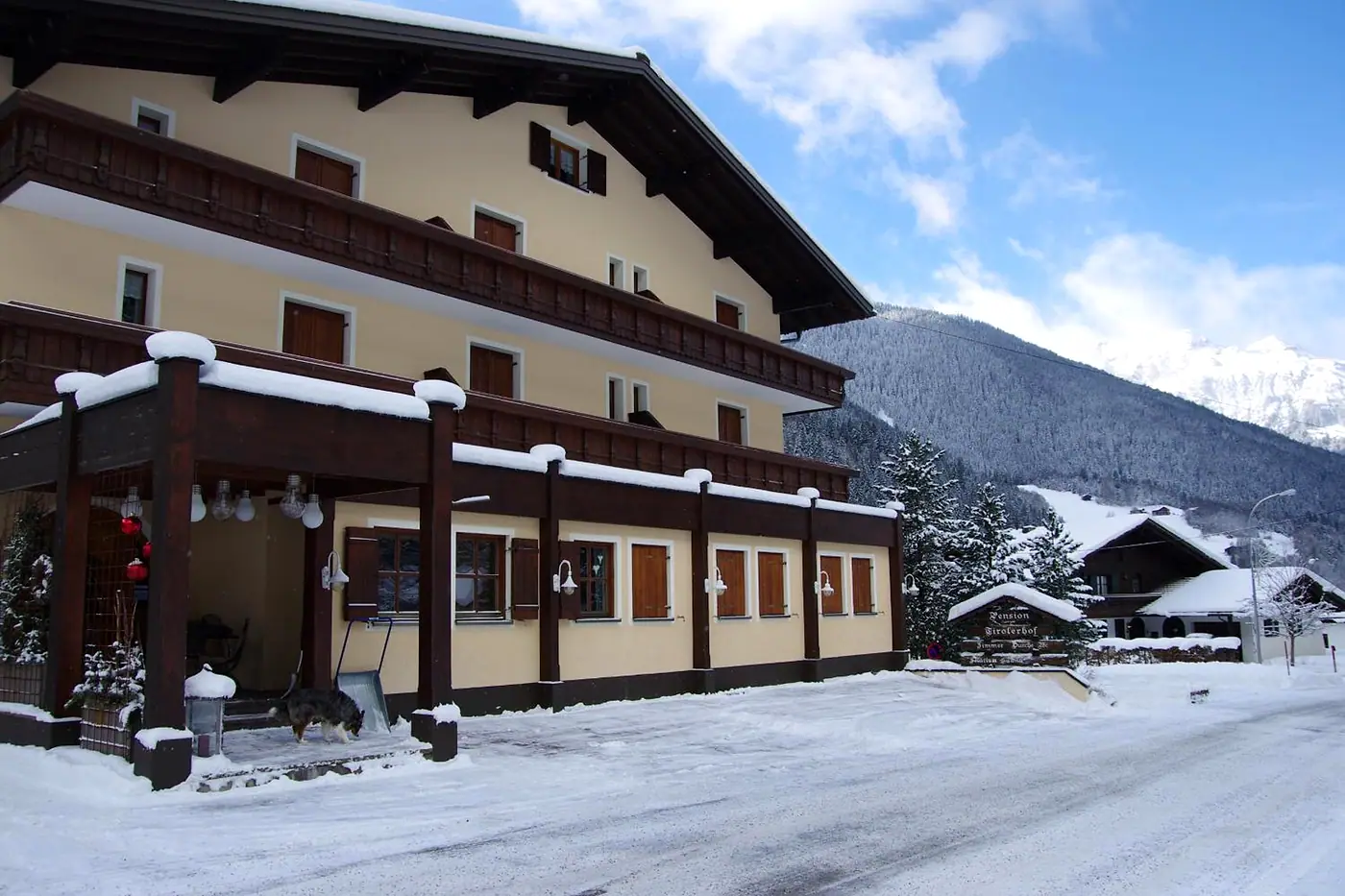 Der Tirolerhof im Winter, verschneit unter blauem Himmel, dahinter die Berge über Partenen